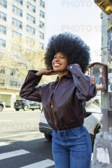 Young african american woman with afro hair smiling confidently on a sunny manhattan street, enjoying urban city life in casual leather jacket and denim, radiant and free