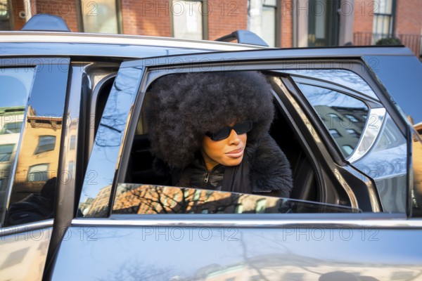 Elegant black woman wearing large sunglasses and an afro hairstyle, looking out of a car window while arriving in manhattan, new york city, capturing urban fashion and city life