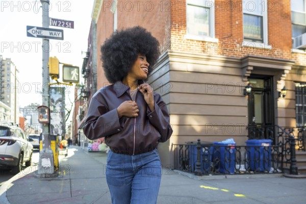 Young black woman with an afro hairstyle smiling while walking along a vibrant w 22nd street sidewalk in chelsea, new york city, enjoying urban travel and lifestyle