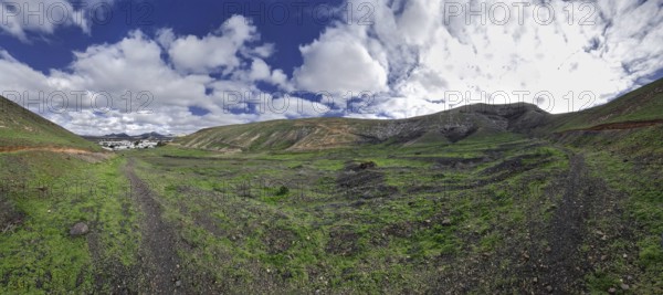 Wide landscape with trails and grassy hills under cloudy sky, Yaiza Lanzarote