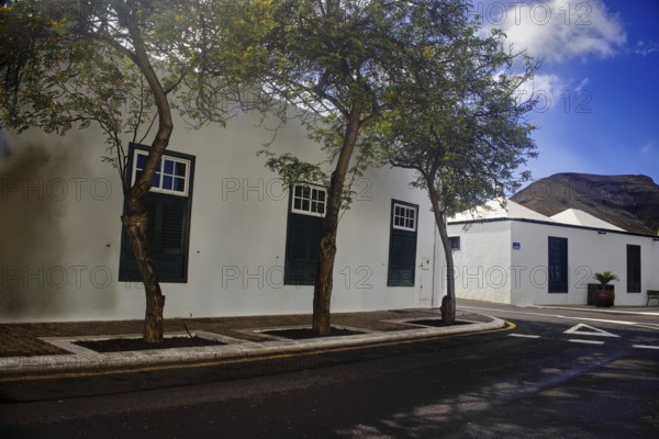 White building with green shutters and trees along the road, Yaiza Lanzarote