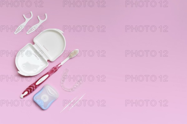 Top view of dental clear aligners, toothbrush, toothpicks and floss on pink background with copy space
