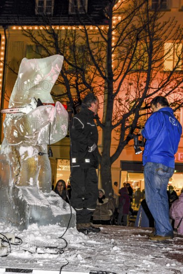Ice carving artist in front of his ice sculpture interviewed by a GEA reporter during ice carving street action as part of the long shopping night in downtown Reutlingen, Baden-Württemberg, Germany, for editorial use only