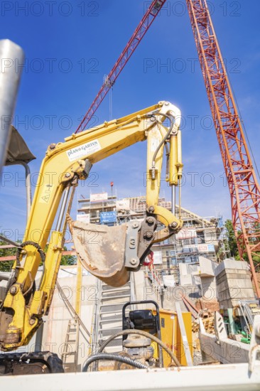 Large yellow excavator on a construction site surrounded by construction cranes, carpentry, new building, Stuttgart, Germany