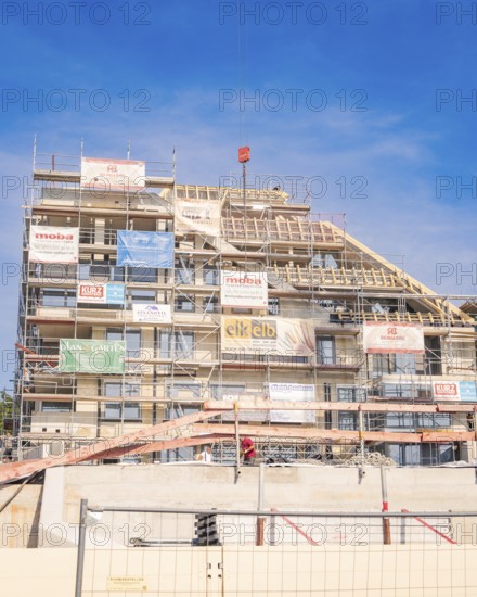 Large building under construction with scaffolding and various advertising banners as well as construction crane, carpentry, new building, Stuttgart, Germany