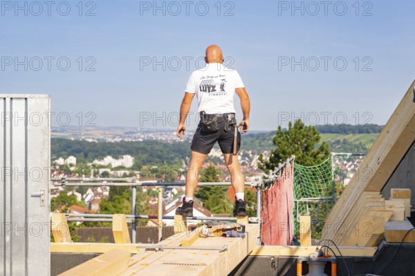 A construction worker on a roof with a view of the urban landscape under bright sky, carpentry, new building, Stuttgart, Germany