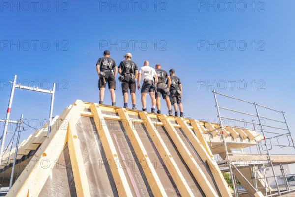 A group of construction workers standing on a roof structure under a blue sky, carpentry, new building, Stuttgart, Germany