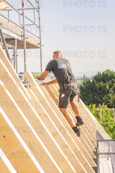 A construction worker climbs up a wooden structure on scaffolding against a blue sky, carpentry, new building, Stuttgart, Germany