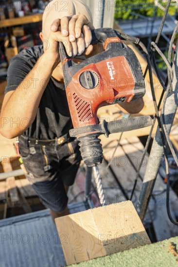 A construction worker wearing a safety helmet uses a drill to drill a hole in a wooden beam, carpentry, new building, Stuttgart, Germany
