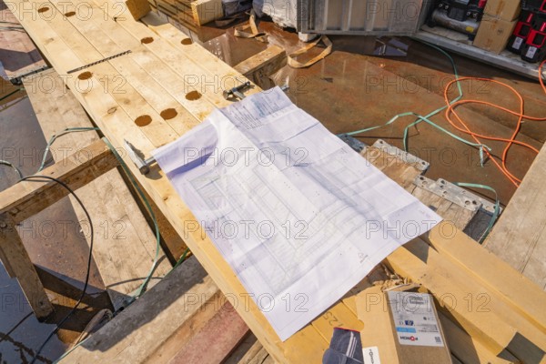A construction plan is lying on wooden planks on a construction site, surrounded by cables and tools, carpentry, new building, Stuttgart, Germany