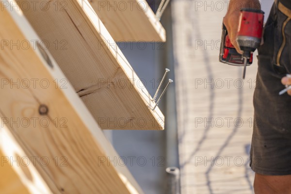 Worker holding drill next to wooden board with screws already screwed in, carpentry, new building, Stuttgart, Germany