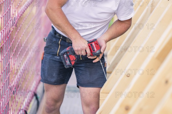 A construction worker uses a screwdriver to work on a wooden structure next to a net, carpentry, new building, Stuttgart, Germany