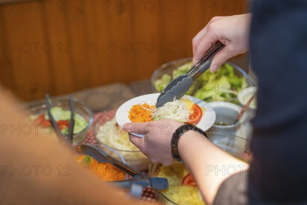Person uses tongs to place fresh raw food on a plate at the buffet