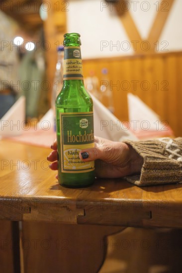 A person holds a beer bottle on a wooden table