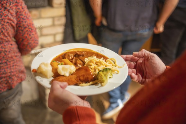 Person holding plates of goulash and spaetzle in a convivial setting