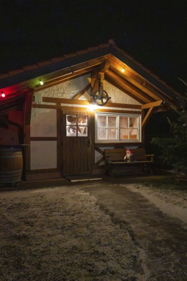 Small wooden hut decorated at night with festive lights and winter accessories