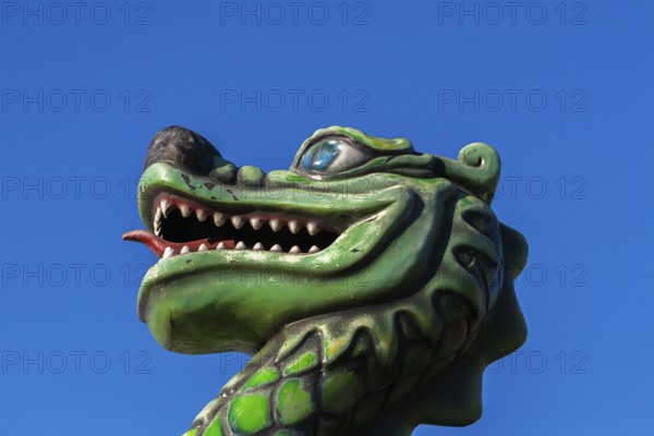 Green dragon with big teeth and long red tongue against blue sky background, Fun Show traveling amusement ride park, Old Port of Montreal, Quebec, Canada