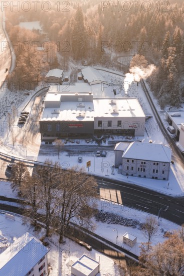 Snowy factory near a forest at sunrise, steam from chimney, Nagold, Calw district, Black Forest, Germany