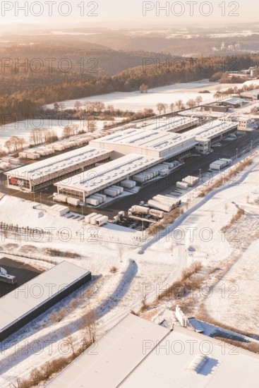 Warehouse with surrounding trucks in snow-covered landscape at morning sun, Nagold, Calw district, Black Forest, Germany
