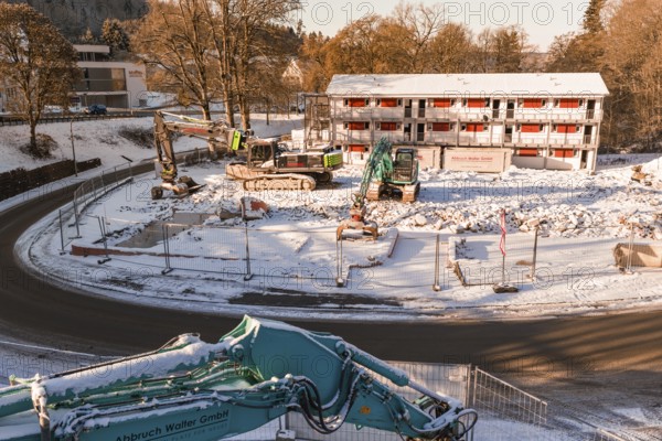 Snow-covered construction site with several excavators and a large building in the background, Nagold, Calw district, Black Forest, Germany
