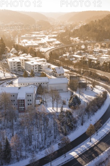 Snowy buildings and roads in an urban landscape surrounded by hills and trees in the morning light, Nagold, Calw district, Black Forest, Germany