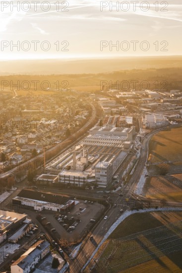 Industrial area and city in winter surroundings, illuminated by sunrise, fields and roads visible, Althengstett, Calw district, Germany