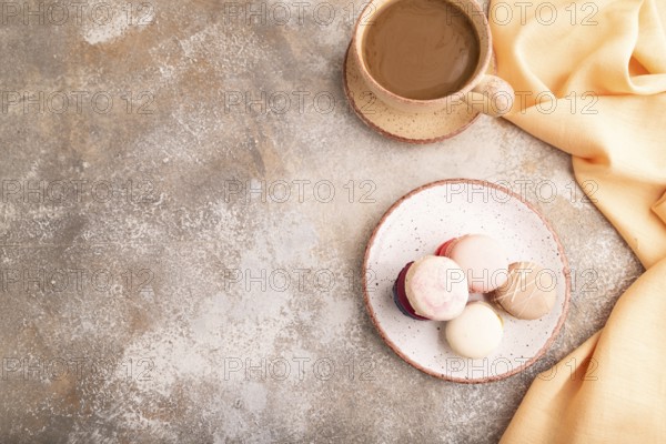 Macarons colourful cookies dessert, cup of coffee, on brown concrete background with orange linen textile, copy space, top view, flat lay