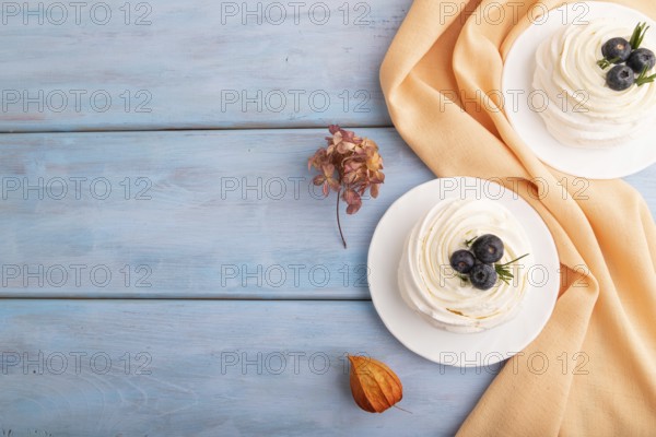 Pavlova Meringue dessert with crisp meringue and blueberry on blue wooden background with orange linen textile, copy space, top view, flat lay