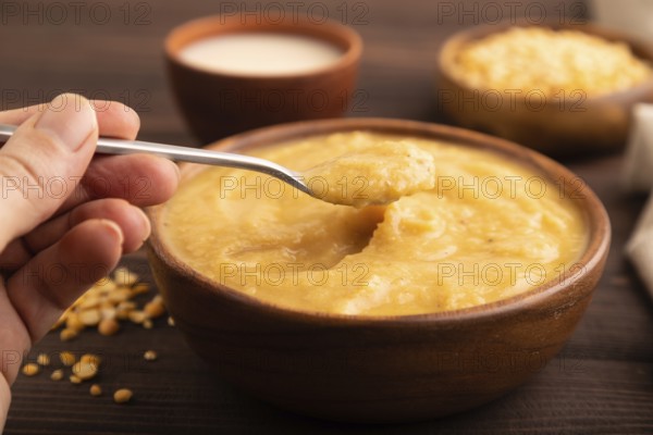 Pea cream soup, Puree, porridge in wooden bowl with hand on wooden background and linen textile. Diet, healthy eating concept. side view, close up, selective focus