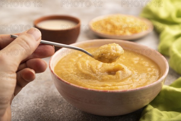 Pea cream soup, Puree, porridge in ceramic bowl with hand on brown concrete background and green linen textile. Diet, healthy eating concept. side view, close up, minimalism, selective focus