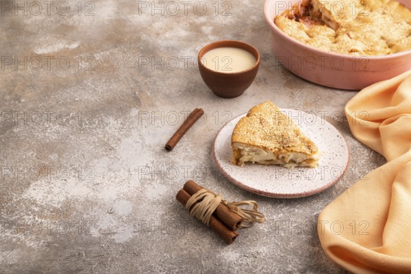 Apple Charlotte cake on brown concrete background and orange linen textile, cup of milk, side view, copy space