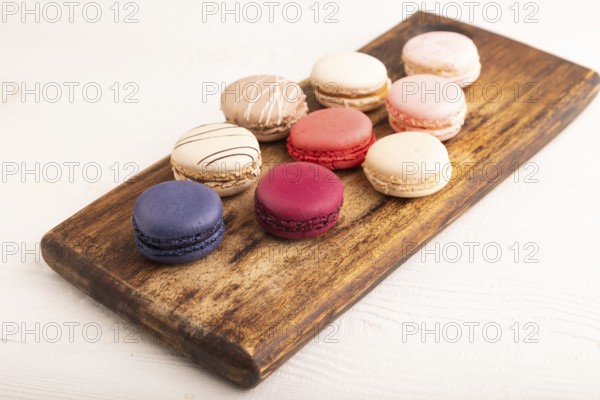 Macarons colourful cookies dessert on brown wooden cutting board on white wooden background, close up, side view