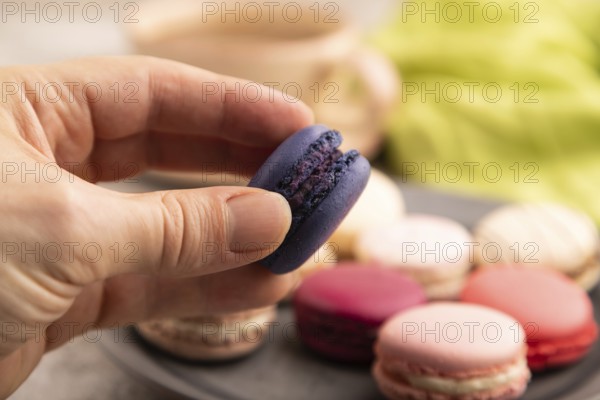Macarons colourful cookies dessert with hand on brown concrete background with green linen textile, close up, side view, selective focus