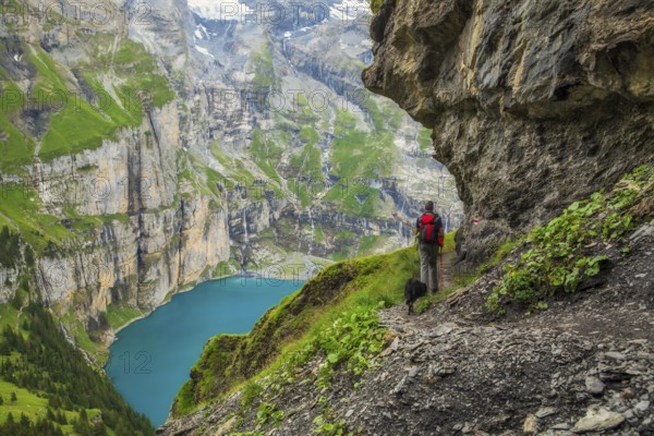On a summer day, a tourist walks along the panoramic trail with views of Oeschinen Lake (Oeschinensee), Bernese Oberland near Kandersteg, Switzerland