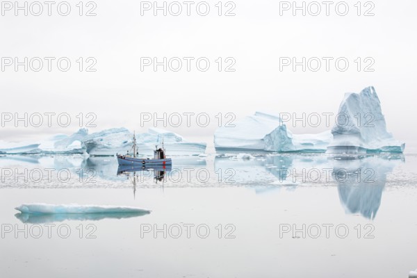 Fisherman's boat navigating near floating icebergs in the bay by Ataa village at sunset, Disko Bay, Arctic, Greenland, geographically part of North America, politically part of the Kingdom of Denmark