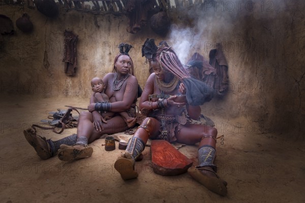 Ovahimba or Himba women, one with a child while another takes a traditional smoke bath, Kaokoland, Kunene Region, Namibia