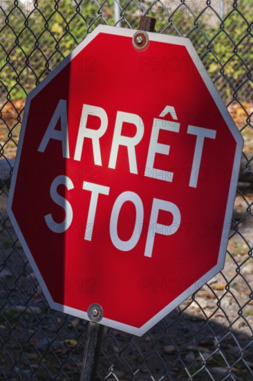 Close-up of bright red bilingual French arret and English stop sign with wire mesh fence in background, Quebec, Canada