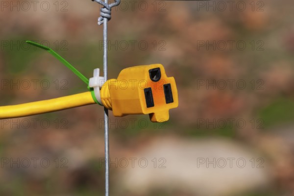 Close-up of yellow female rubber connector power plug attached to wire mesh fence with plastic tie wraps, Quebec, Canada