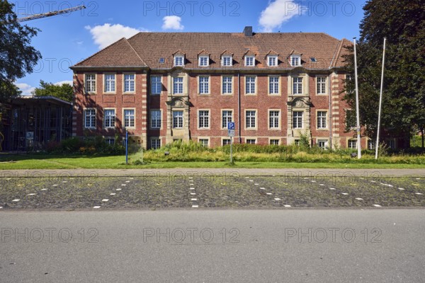 Town hall, brick buildings, flagpoles, façade with windows, dormers, parking boxes, sidewalk, asphalt road, paving stones, meadow, trees, blue sky, cumulus clouds, Im Piepershagen, Borken, Münsterland, Borken district, North Rhine-Westphalia, Germany