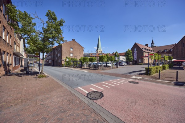 Residential building, brick building, general architecture, church tower of St. Remigius, sidewalk, street, barrier bollard, parking lot with cars, trees, blue sky, cloudless, Brinkstraße, Borken, Münsterland, Borken district, North Rhine-Westphalia, Germany