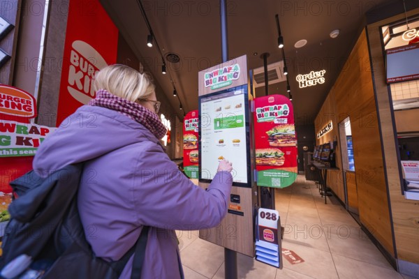 A woman interacts with an ordering machine in a modern fast food restaurant, London, England, Great Britain