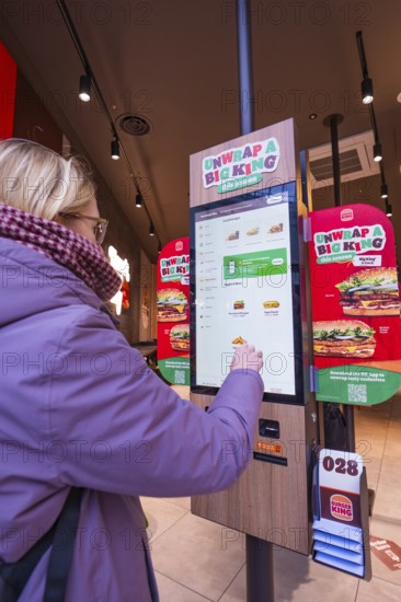 A woman uses an ordering machine in a modern burger restaurant, London, England, Great Britain