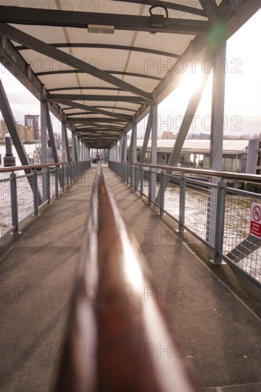A modern metal footbridge stretches across a river in sunlight, London, England, Great Britain