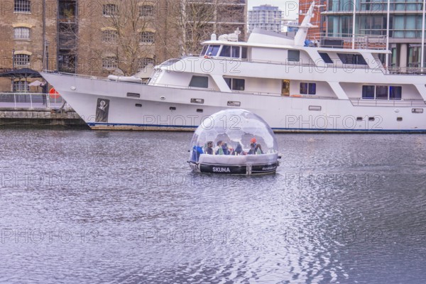 A boat with a glass dome on a body of water next to a large yacht in the harbor, London, England, Great Britain