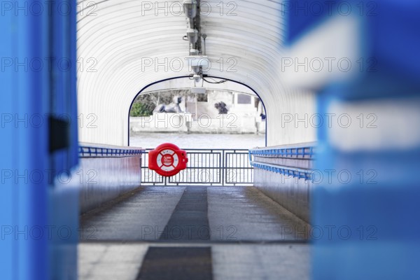 A modern passageway leads to a river, accented with a blue lifebuoy, London, England, Great Britain