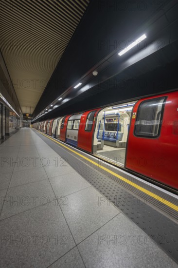 An incoming red subway train stands at an illuminated platform in a dark train station, London, United Kingdom
