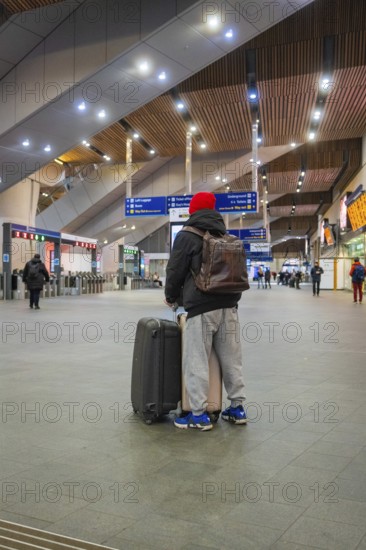 A person in a train station with luggage, modern interior and signpost in the background, London, England, Great Britain