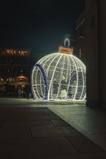 Large glowing Christmas ball on square with people in the evening setting, London, England, Great Britain