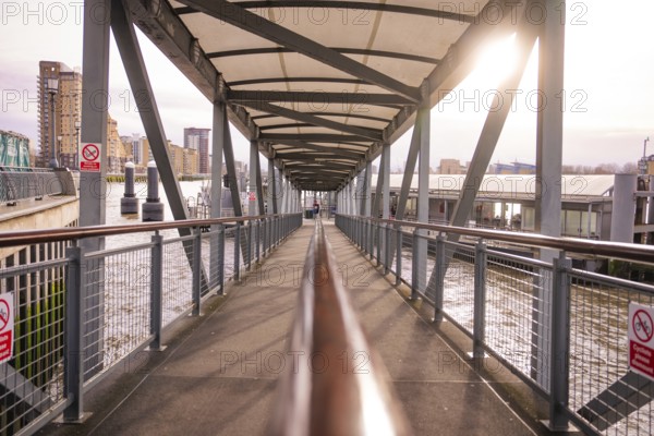 A modern steel bridge with a roof in an urban area, facing the sun, London, England, Great Britain