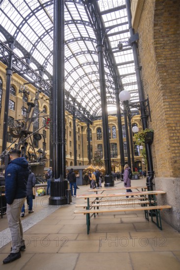 Interior with beer benches and people surrounded by vaulted brick walls and a glass roof, London, United Kingdom